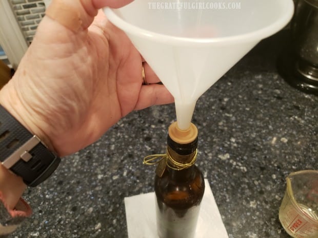 A funnel is used to add the garlic-infused olive oil to a bottle for storage.