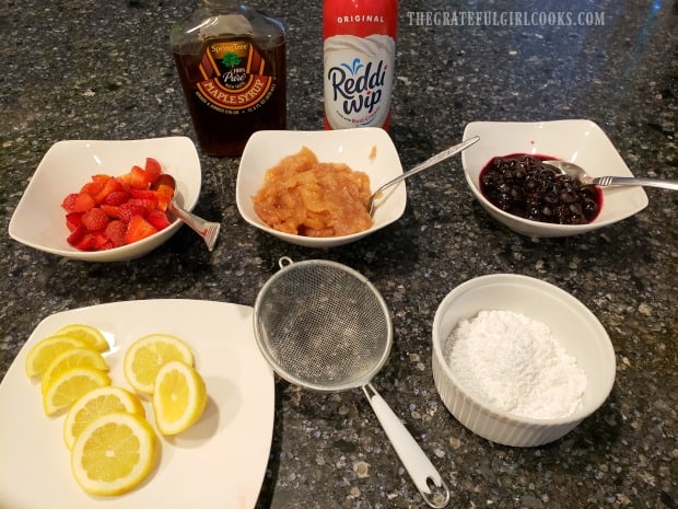 Strawberries, apple pie & blueberry fillings, lemon, powders sugar, whipped cream and syrup ready for Dutch babies.