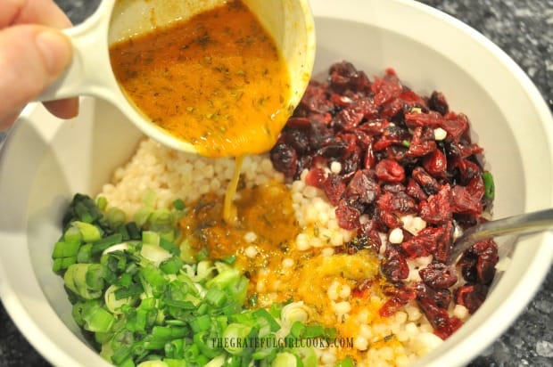 The orange herb vinaigrette is poured on an Israeli couscous salad and then tossed.