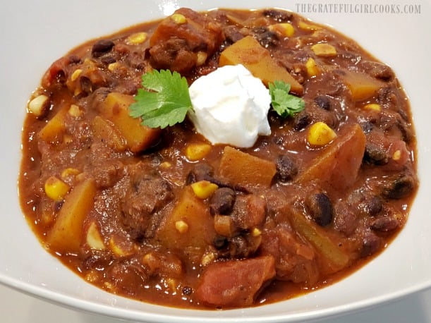 A bowl of black bean butternut squash chili garnished with cilantro and sour cream.