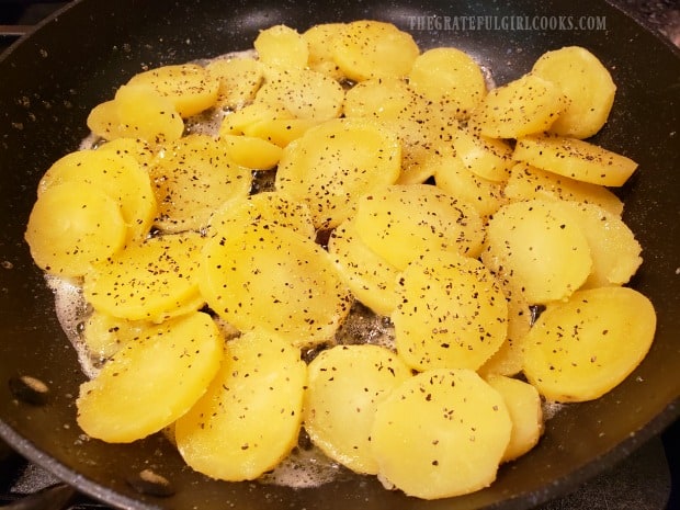 Seasoned, round potato slices are cooked in butter in a skillet.