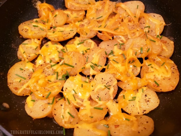 Cheesy skillet potatoes are topped with grated cheese and chopped fresh chives.
