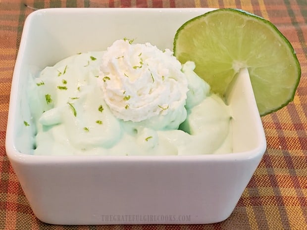Creamy lime mousse is garnished with lime zest, whipping cream, and a slice of lime.