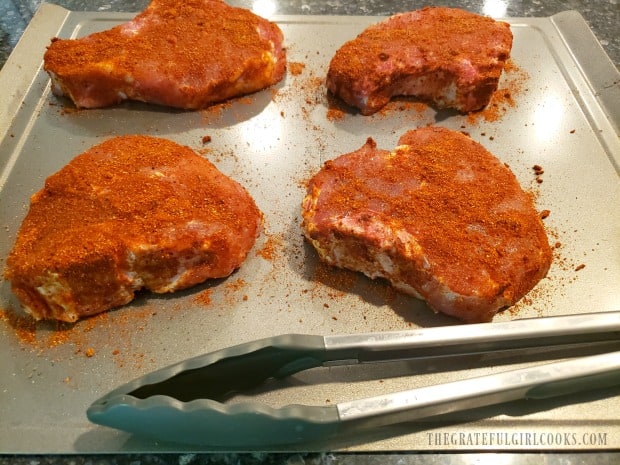 Four bone-in pork chops coated with dry rub spice mix, and ready to grill.