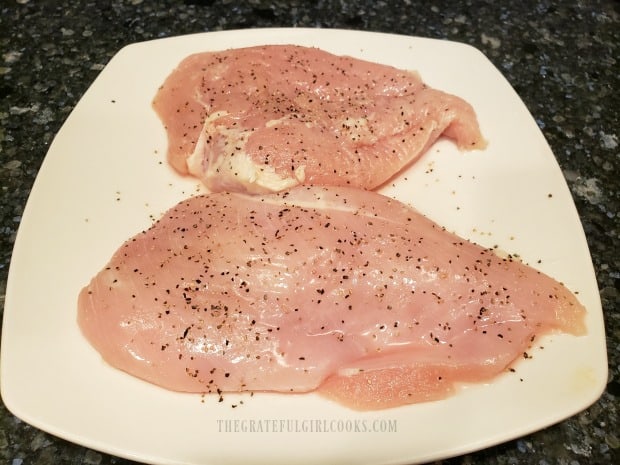 Chicken breasts on white plate, seasoned with salt, pepper, and garlic powder