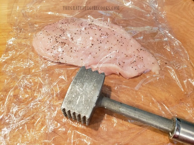The chicken breasts in plastic wrap are pounded thinner with a meat mallet.