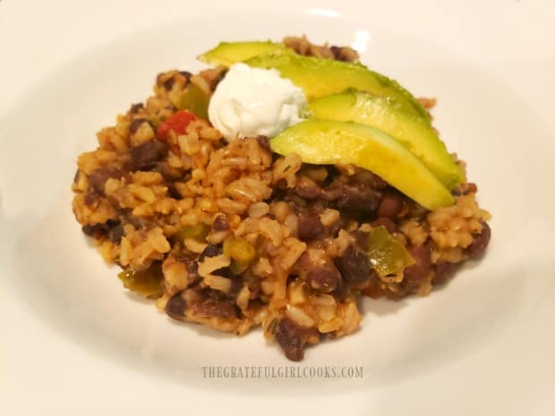 Black beans and rice is served, topped with sour cream and avocado slices.