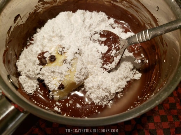 Powdered sugar, butter and water are added to melted chocolate in pan.
