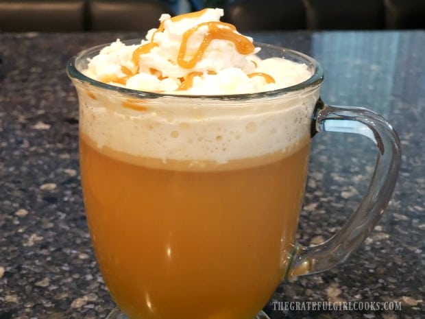 A mug of caramel apple cider, topped with whipped cream and caramel sauce.