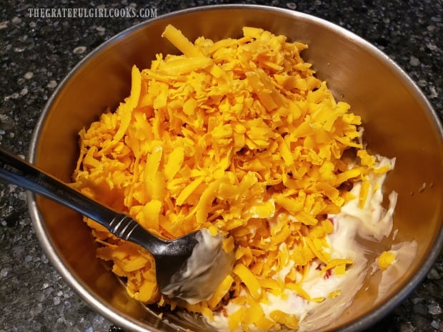 Grated sharp cheddar cheese is added to the ingredients in the mixing bowl.
