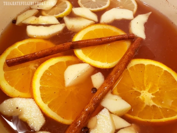 Apple cider, with juices, orange, apple and lemon slices, and cinnamon sticks heating.