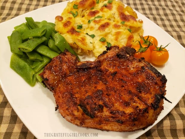 A plate with a pork chop, green beans, tomatoes and Scalloped Potatoes For Two.