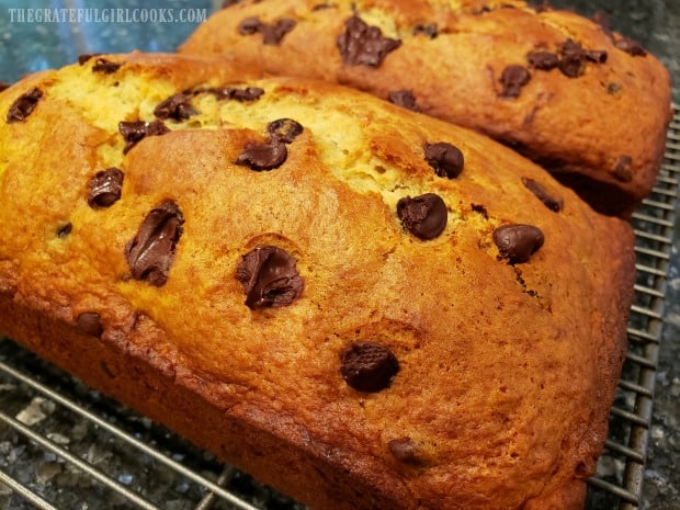 Two loaves of chocolate chip banana bread cool on wire racks after baking.