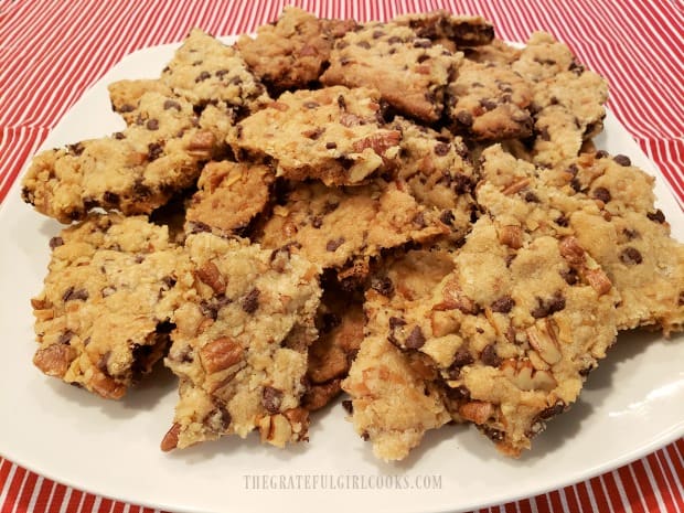 A white platter full of pieces of chocolate chip pecan brittle.
