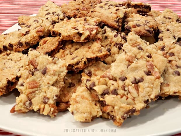 There are many sizes and shapes of chocolate chip pecan brittle on the plate.
