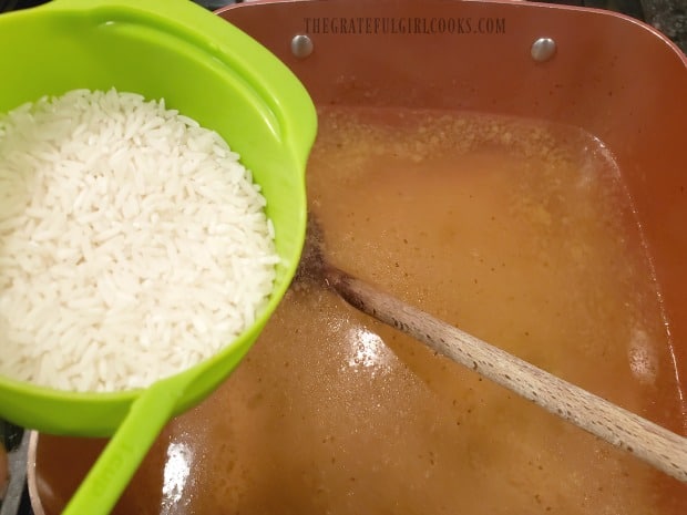 Uncooked rice is added to boiling chicken broth to cook.