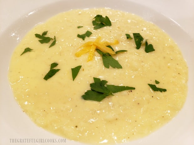 A bowl of Creamy Avgolemono Soup, garnished with chopped parsley and lemon peel.