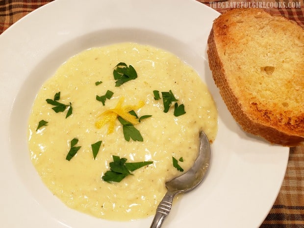 Garlic bread served on the rim of a bowl of creamy avgolemono soup.