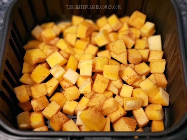 Air fryer basket with cubes of butternut squash, ready to cook.