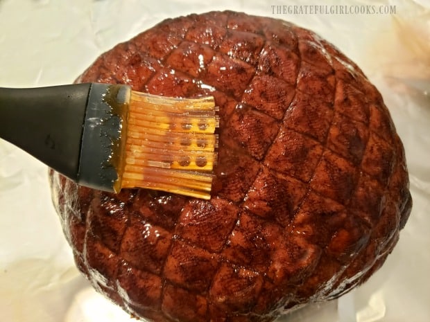 A ham is place on aluminum foil, then coated with brown sugar glaze.