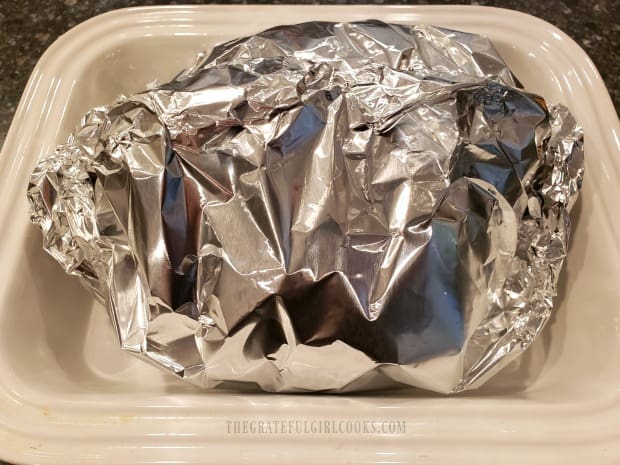 Aluminum foil tightly seals the brown sugar glazed ham for baking.