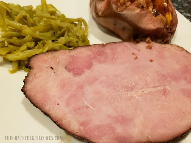 Green beans and a sweet potato are served with a brown sugar glazed ham slice.