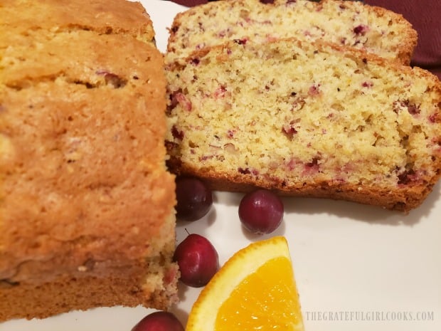 Two slices of cranberry orange bread and remaining loaf on a white plate.