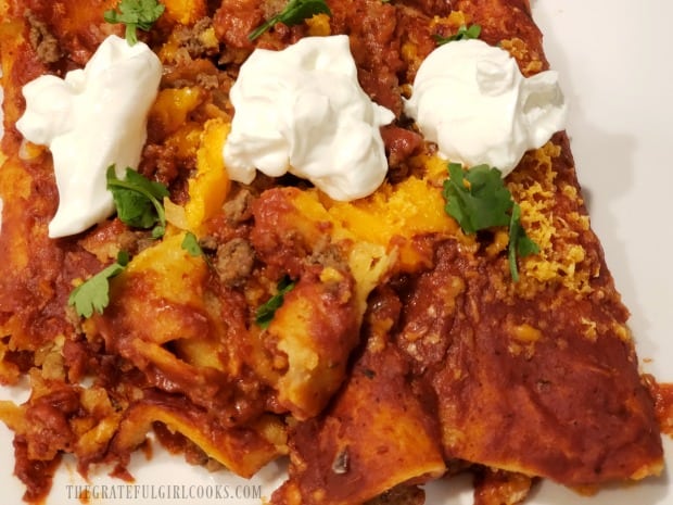 Baked enchiladas ready to serve, garnished with sour cream and cilantro.
