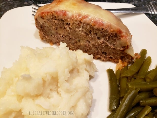A slice of cheesy Italian meatloaf served with mashed potatoes and green beans.