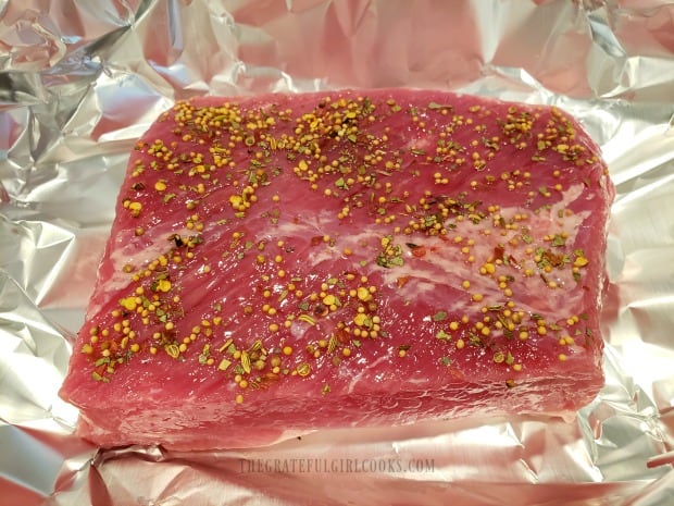 Spices cover the surface of a corned beef, ready for baking.