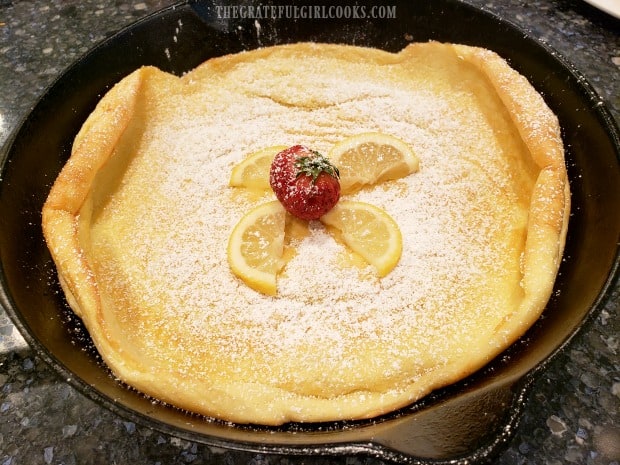 A lemon Dutch baby, garnished with powdered sugar, lemon wedges and a strawberry.