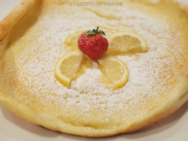 Lemon wedges and a strawberry garnish the powdered sugar covered Lemon Dutch Baby.