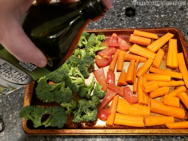 The vegetables are drizzled with olive oil before seasoning.