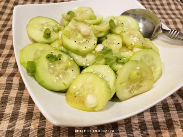 Asian Cucumber Salad is served garnished with sesame seeds in a white bowl.