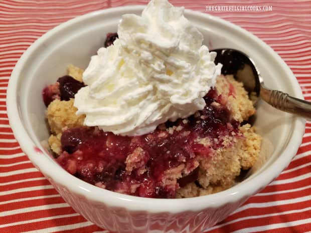 A small bowl of blueberry cranberry crisp, topped with whipped cream.