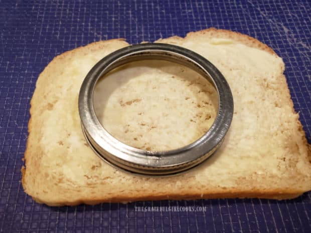 A jar or jar lid is used to cut out a circle in buttered bread.