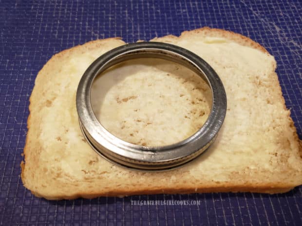 A jar or jar lid is used to cut out a circle in buttered bread.