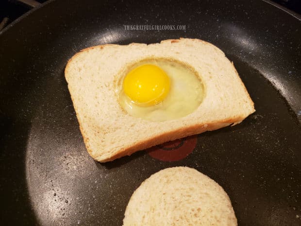 Butter is added to hole in bread, then an egg is cracked into hole.