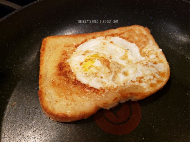 After cooking for a couple minutes, the egg in a basket is flipped to other side.