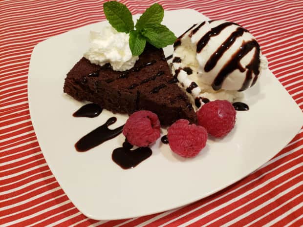 Flourless chocolate cake is served with ice cream, raspberries, and chocolate syrup.