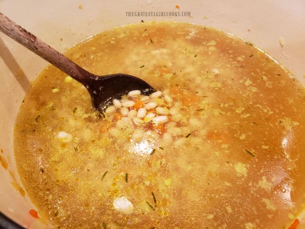 Chicken stock, navy beans and seasonings are cooked in soup pot.