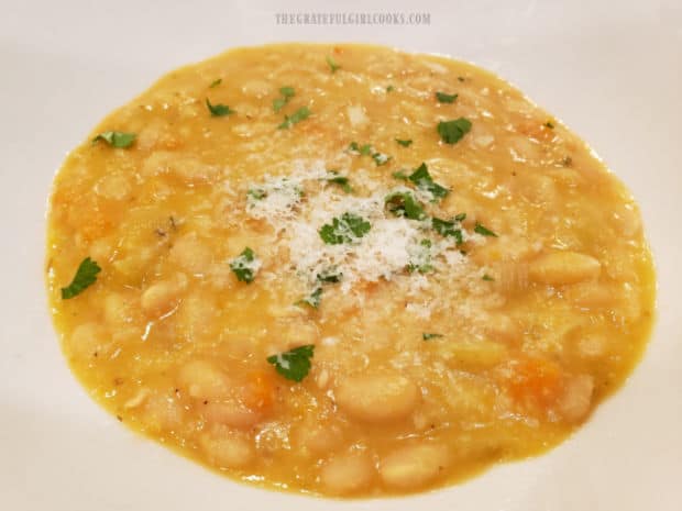 Bowl of navy bean soup, garnished with Parmesan cheese and parsley.