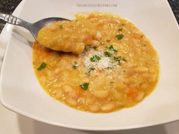 Taking a spoonful of thick navy bean soup from a white bowl.