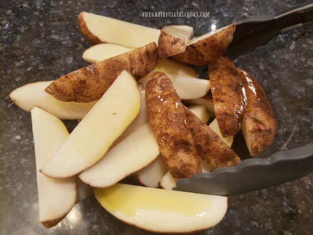 Potato wedges are drizzled with olive oil, and tossed to coat.