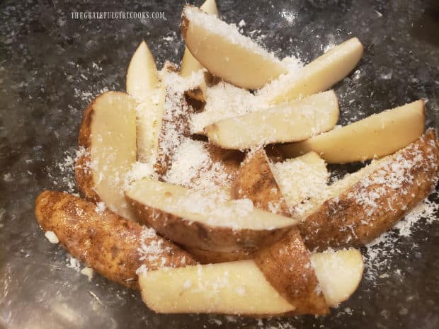 Grated Parmesan cheese is added to, and tossed with the potato wedges.