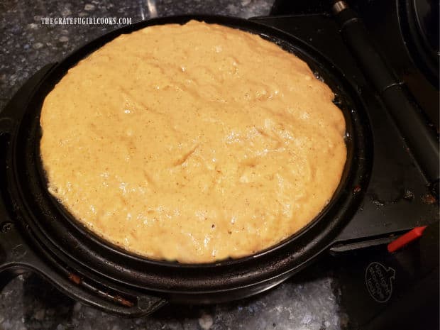 One of the pumpkin spice waffles cooking in a waffle iron.