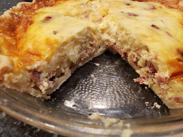 A slice of quiche is removed, revealing bacon and onions inside.