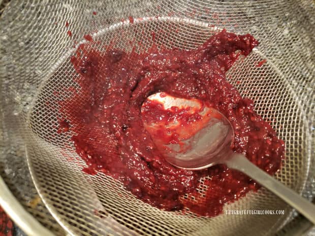 Back of a spoon is used to press cooked blackberries through sieve to filter out seeds.