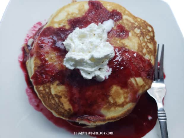 A stack of pancakes topped with homemade blackberry pancake syrup and whipped cream.