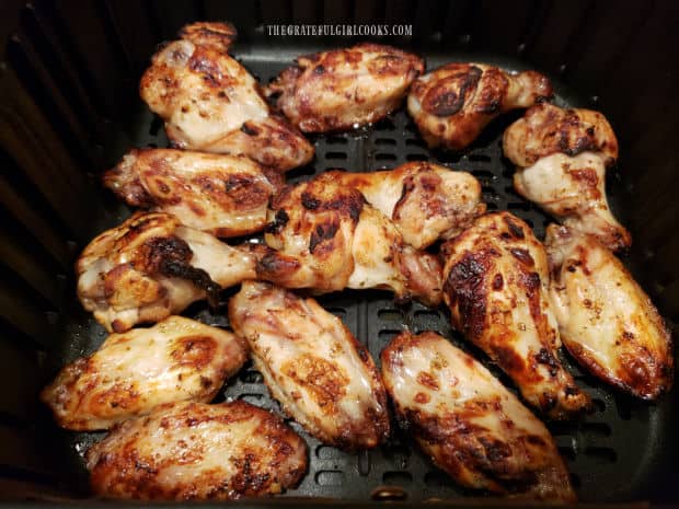 Greek-style chicken wings cooking in air fryer after marinating in sauce.